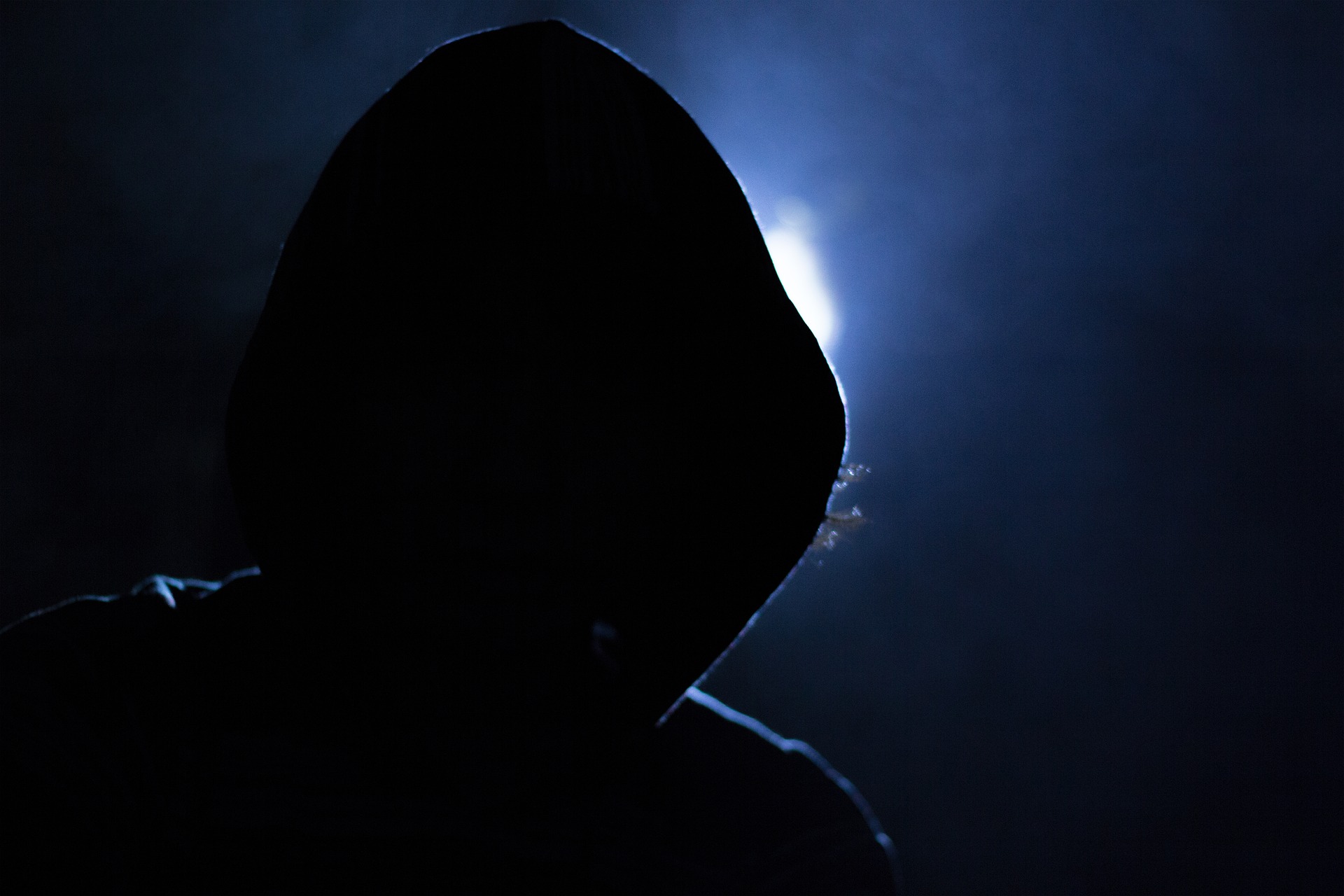 Hooded figure shilouetted in front of a blue light